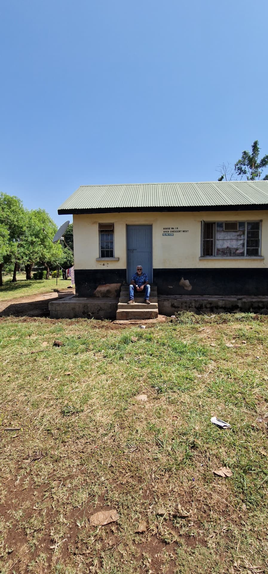 A man seated on the steps of House No. 1B in front of the blue door