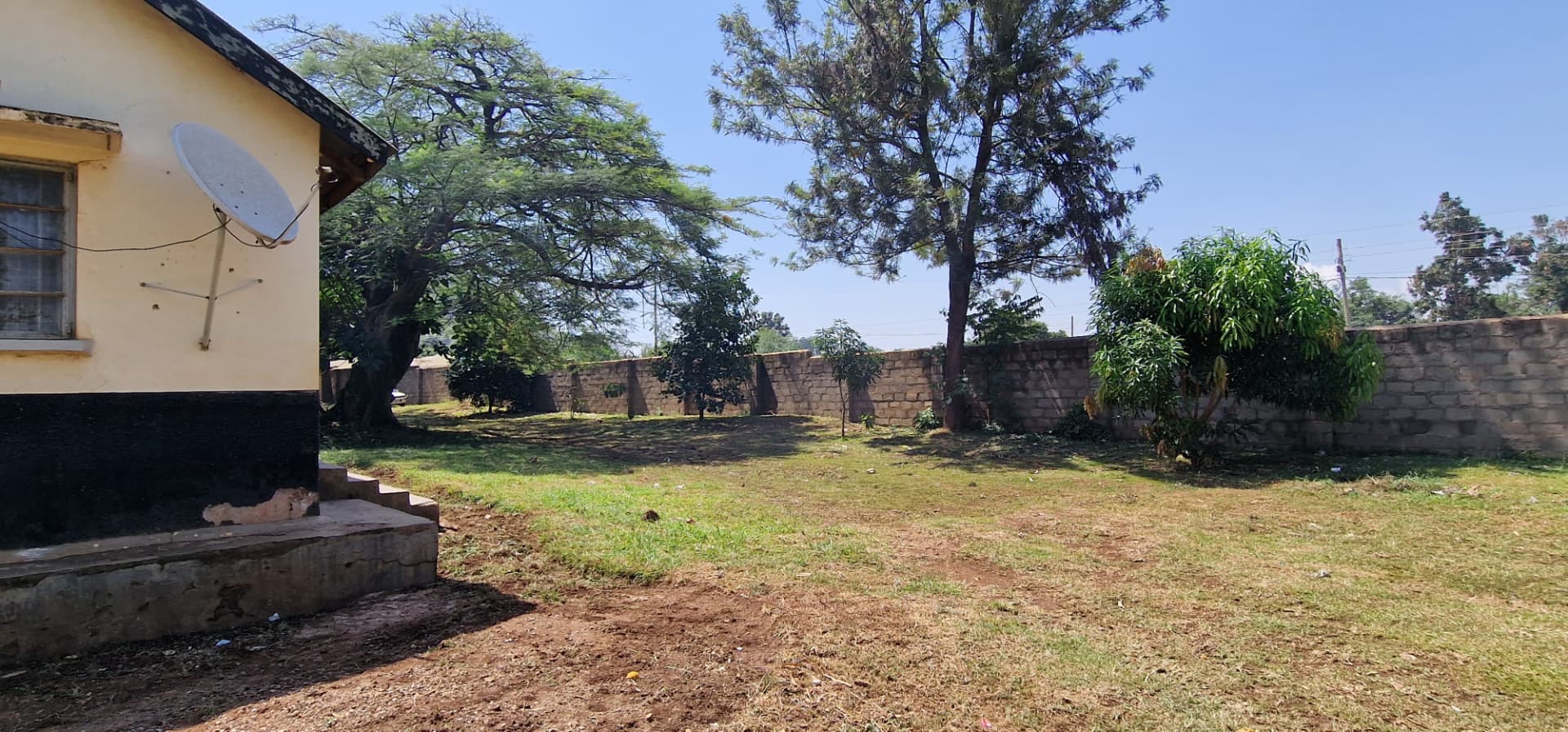 The compound beside the house, bounded by a stone wall and trees